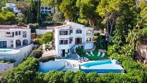 Una villa grande y blanca con piscina, rodeada de exuberante vegetación y árboles.