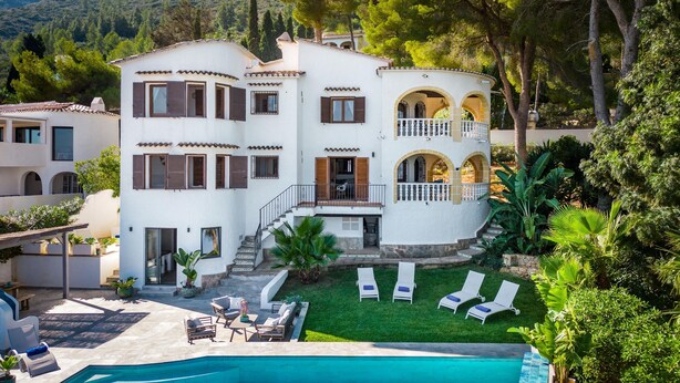 Una villa de varios pisos con piscina, mobiliario exterior y jardín.