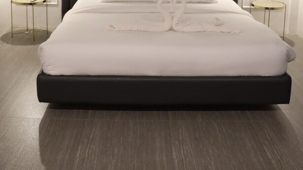 A modern hotel room with a large bed, dark headboard, and two bedside tables with lamps. - H Mansion Hotel (Tandag)