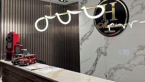 A modern hotel lobby with a marble reception desk, a decorative wall with a logo, and a unique ceiling design. - H Mansion Hotel (Tandag)