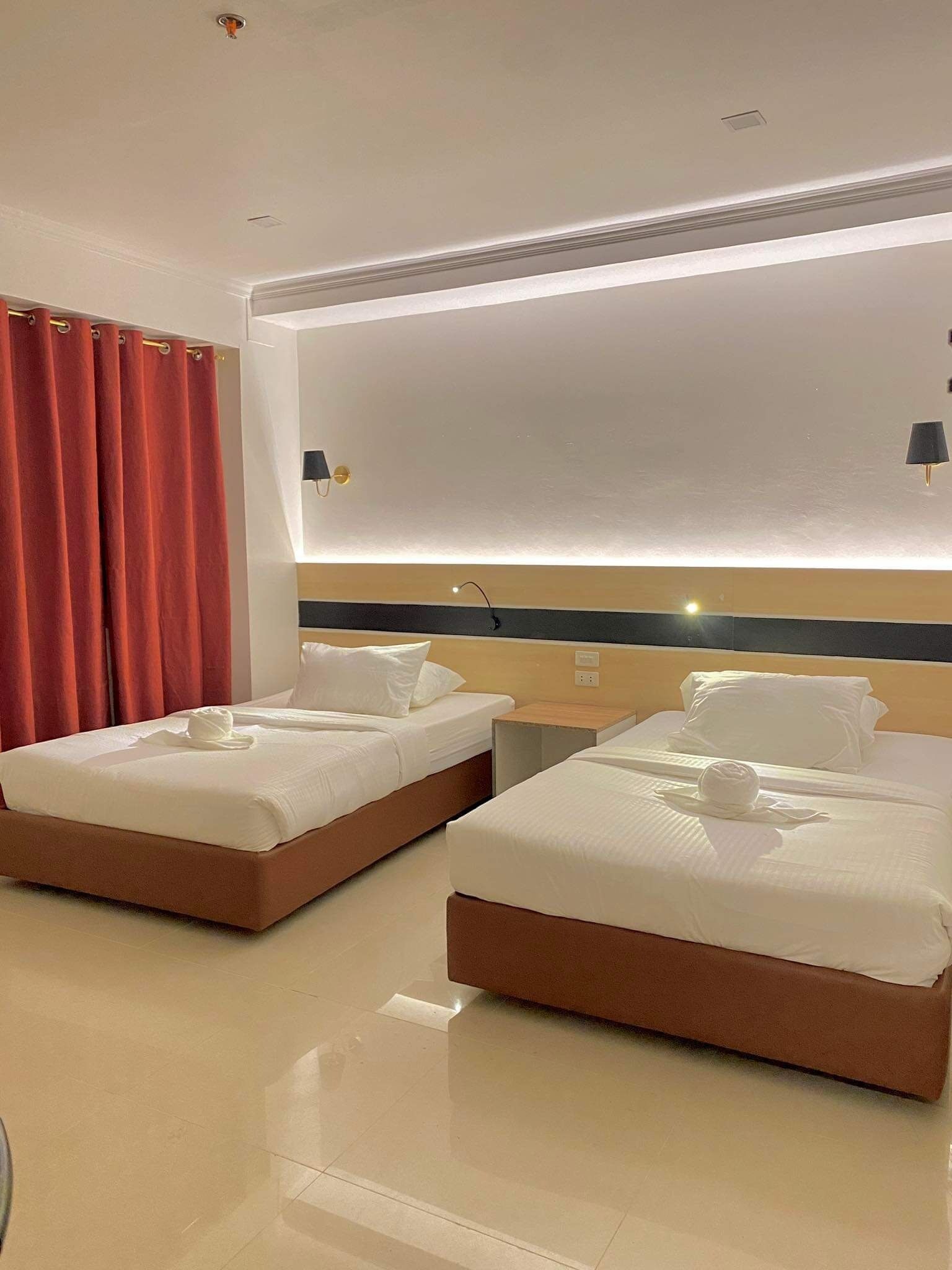 A hotel room with two beds, a large mirror, and a red curtain.