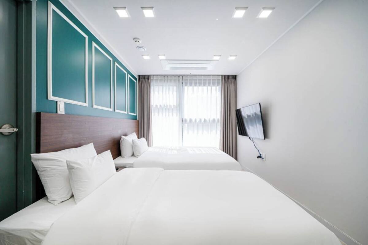 A hotel room with two beds, a TV, and a window with curtains.