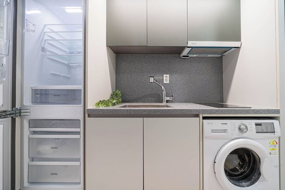 Una cocina compacta con lavadora integrada, un lavamanos y una pequeña encimera.