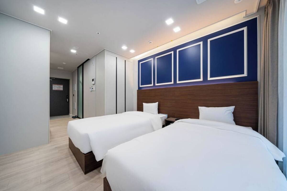 A hotel room with two beds, a wooden headboard, and a white wall with framed panels.