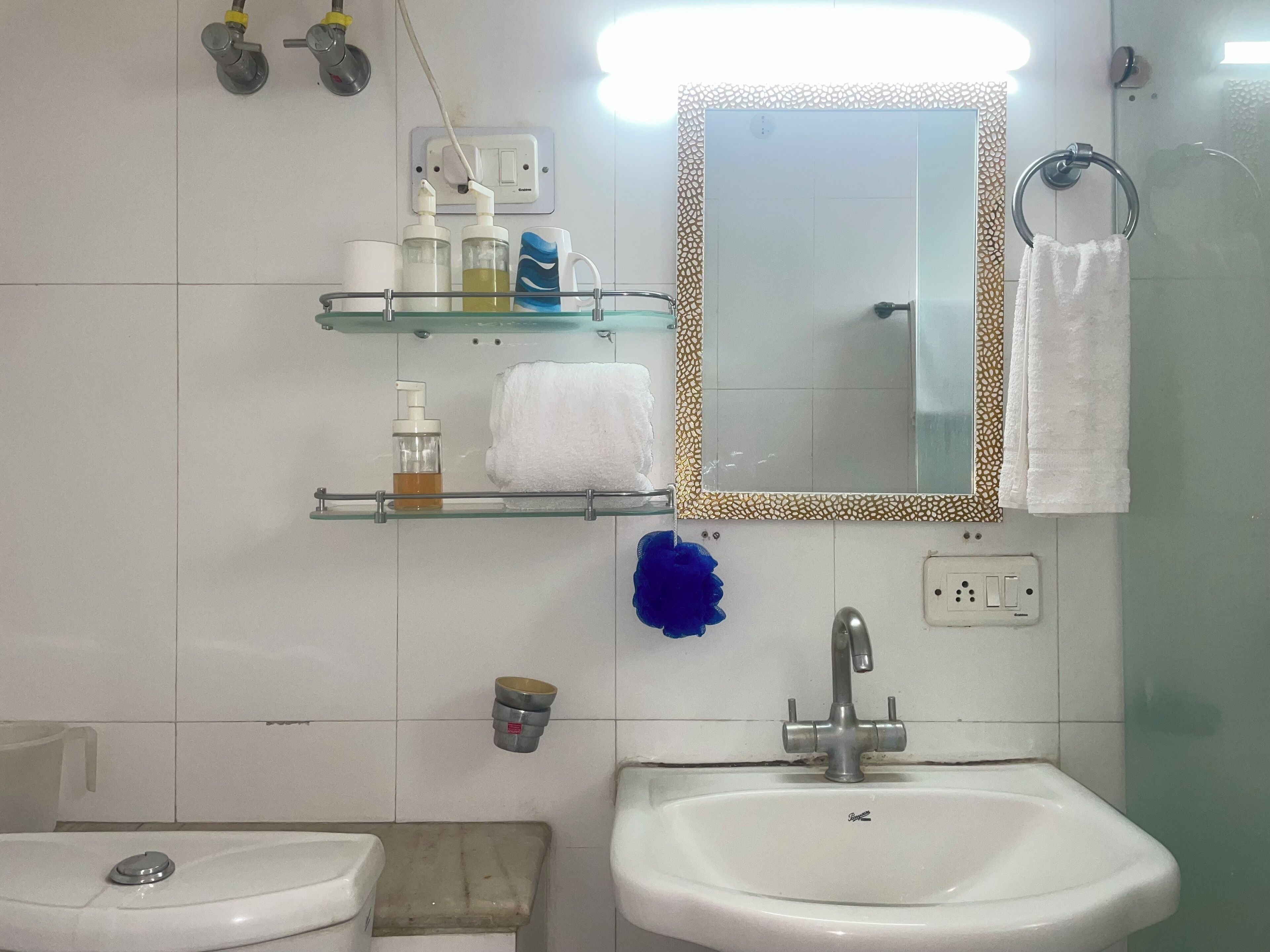 A bathroom with two sinks, a mirror with a decorative frame, a towel rack, and a shelf with toiletries.