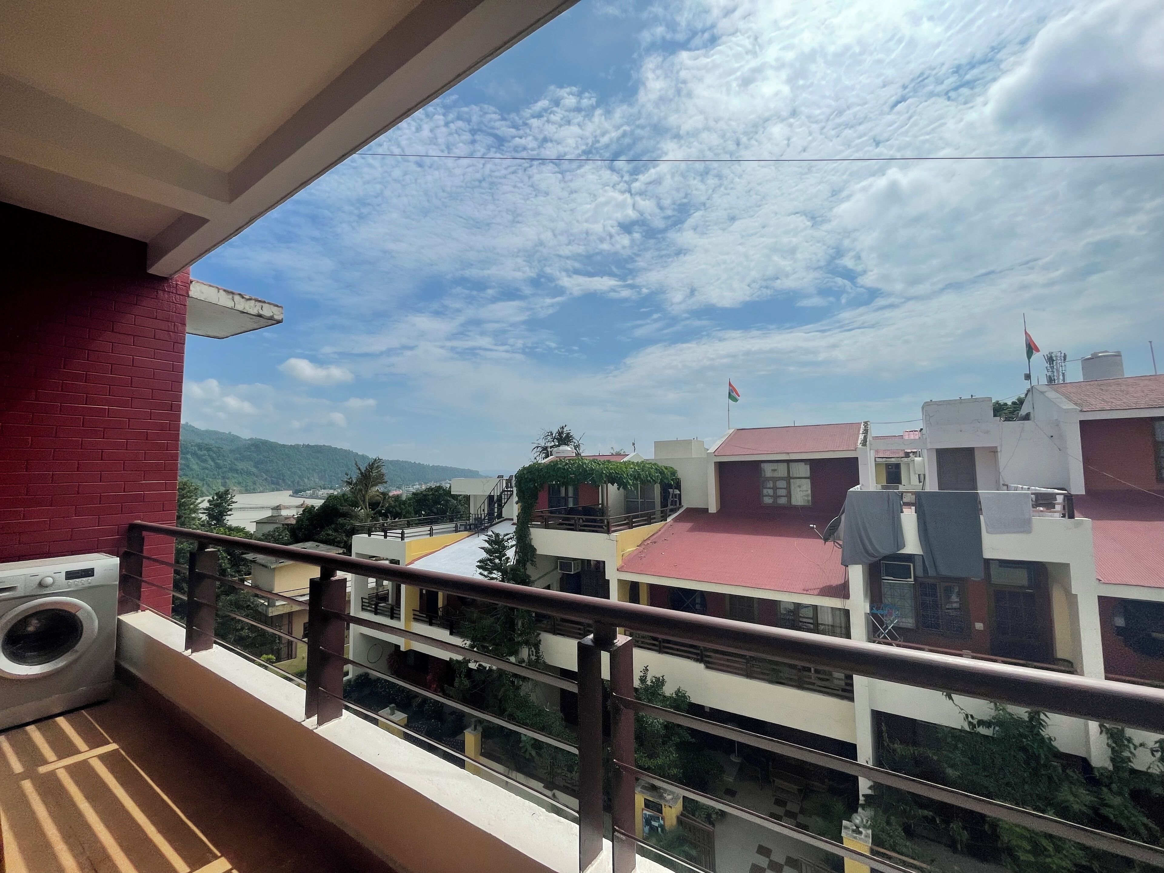 A balcony with a washing machine, a view of a river, and buildings with red roofs.