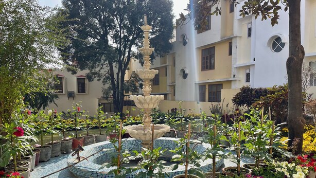 Un patio con una fuente central, rodeado de plantas en macetas y un suelo de baldosas.