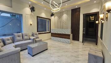 Una sala de estar moderna con un sofá seccional, un otoman y una pared decorativa de mármol.