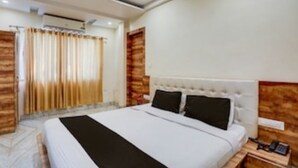 Een hotelkamer met een groot bed, een houten hoofdbord, een nachtkastje met een telefoon en een gordijn voor het raam.