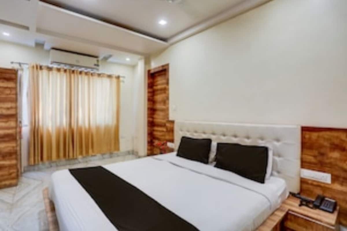 A hotel room with a large bed, a wooden headboard, a bedside table with a phone, and a curtain on the window.