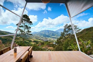 A wooden table with a vase, a bench, and a view of a valley with mountains and trees. - Luxcamp Dieng by Horison (Kejajar)