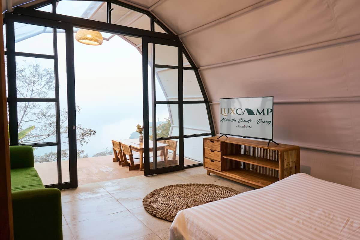 A tented room with a bed, a wooden dresser, a woven rug, and a table with chairs.