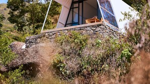 A modern tent-like structure with a stone base, large windows, and a view of the surrounding landscape. - Luxcamp Dieng by Horison (Kejajar)
