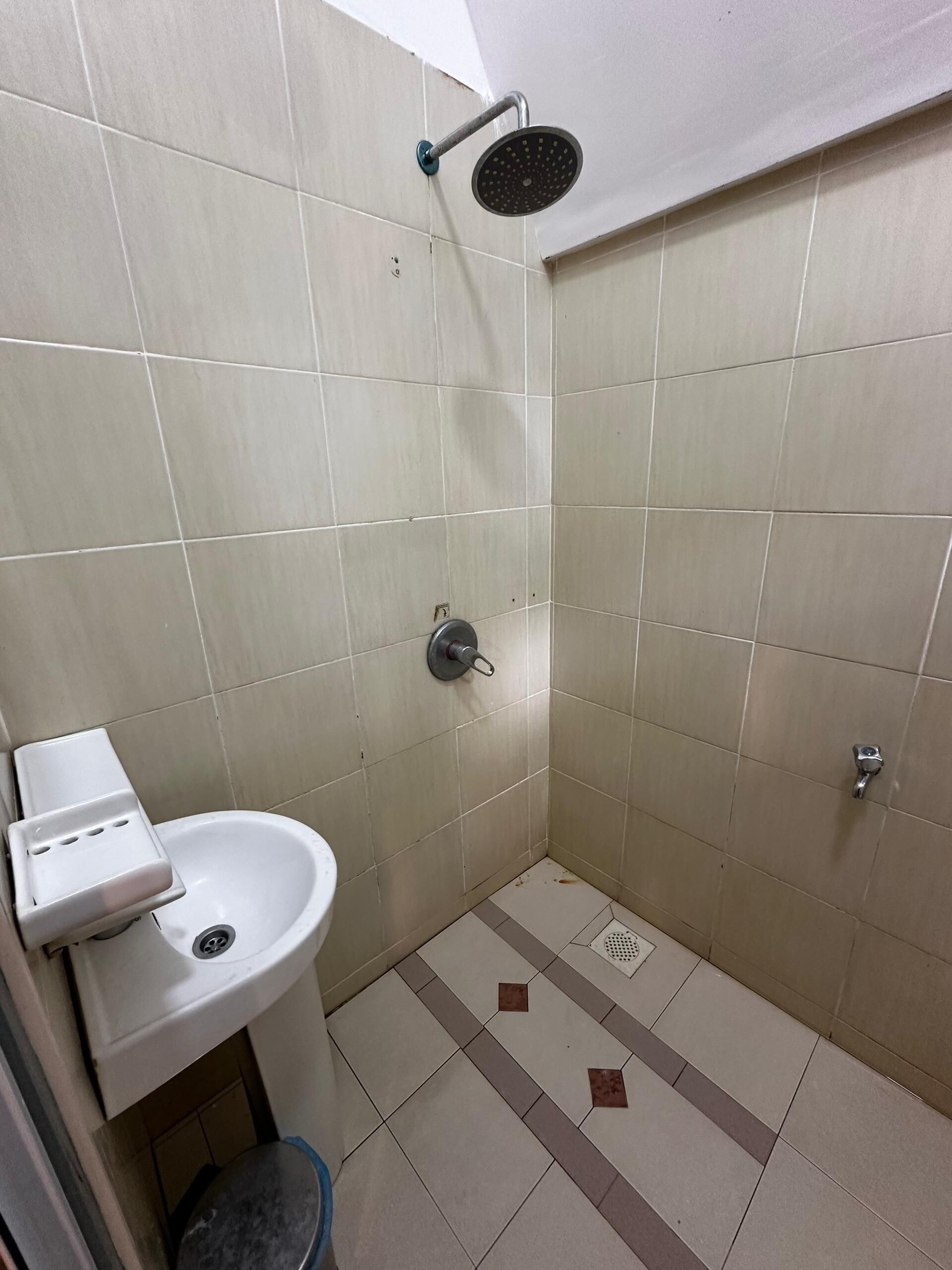 A small, tiled bathroom with a shower, a sink, and a trash bin.