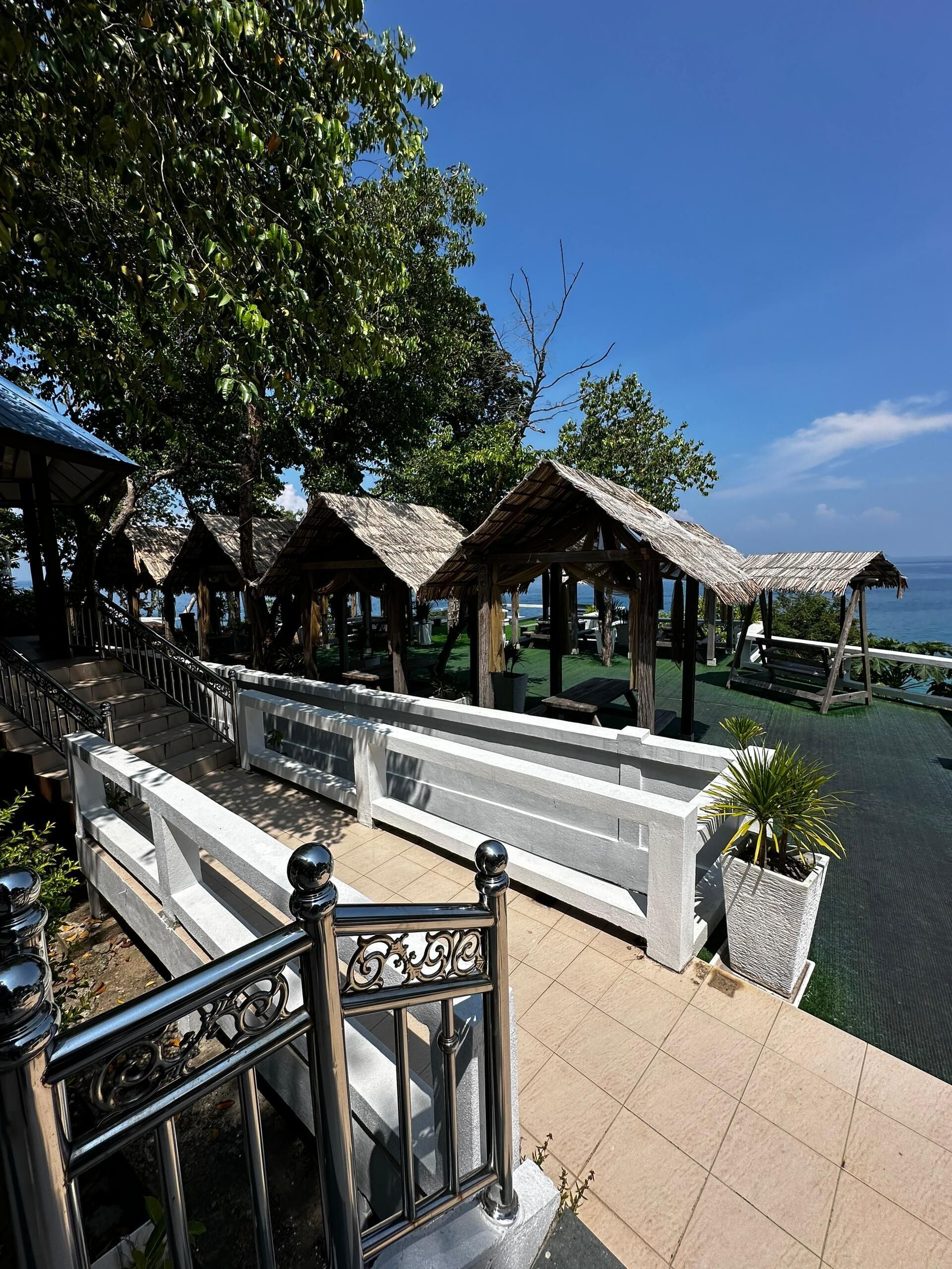 A terrace with a metal railing, a staircase, and thatched-roof structures.