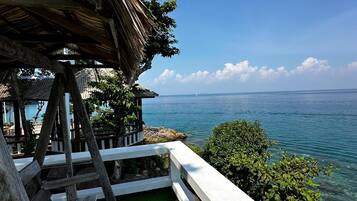 A wooden deck with a thatched roof overlooking a clear blue sea.