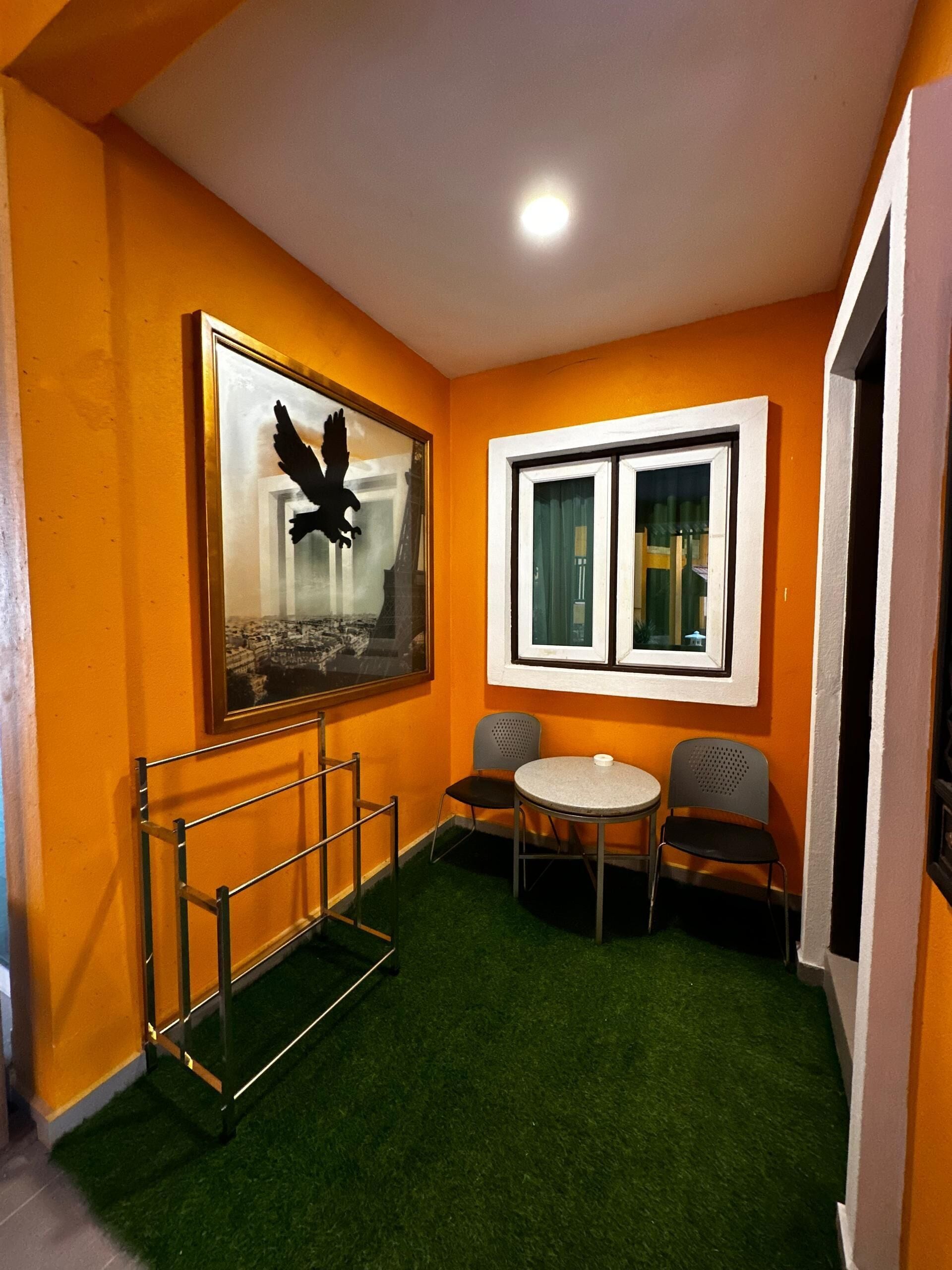 A room with orange walls, a framed picture of a bird, a small round table, two chairs, and a metal rack.