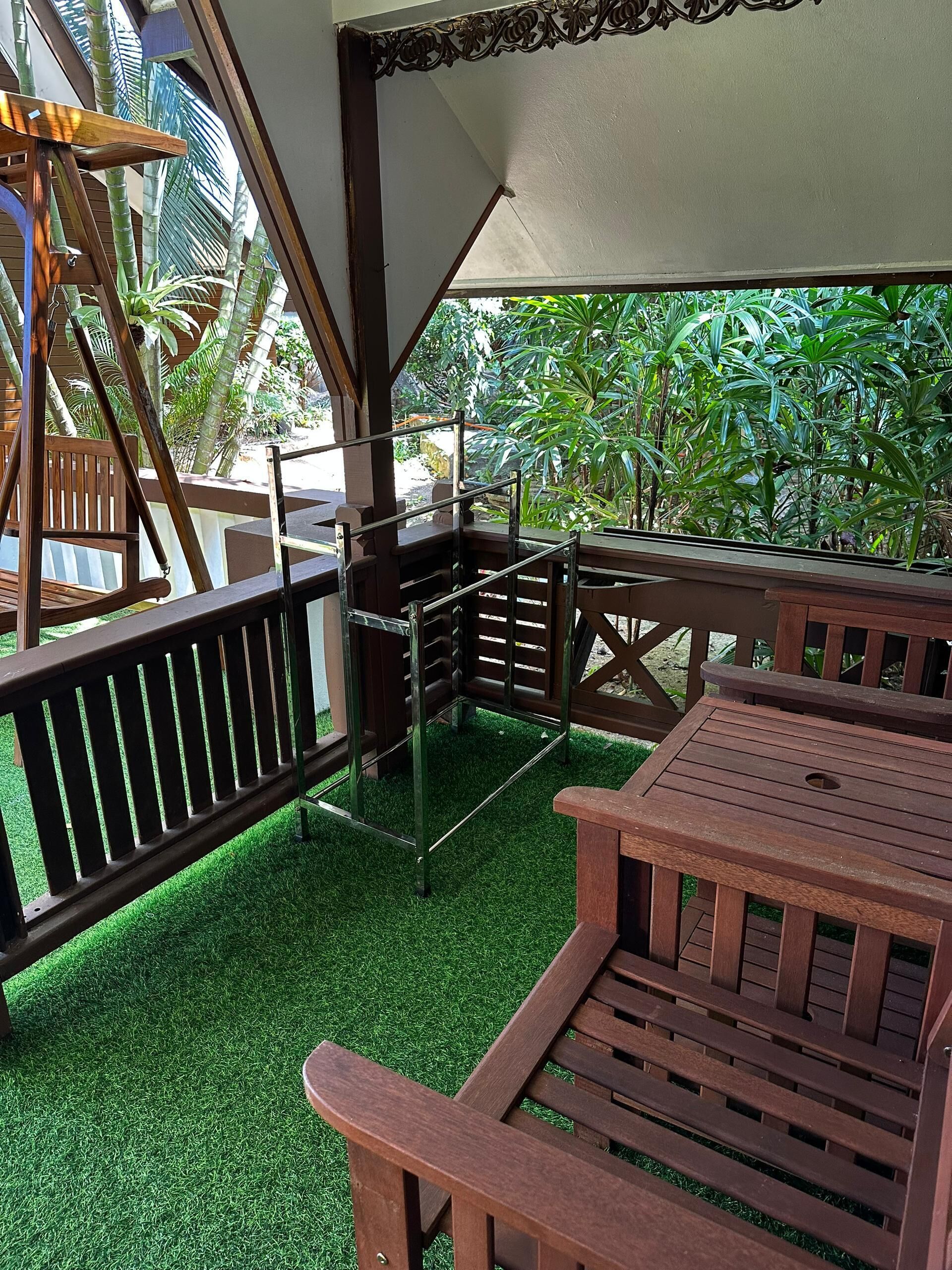 A covered outdoor seating area with wooden furniture and a view of lush greenery.