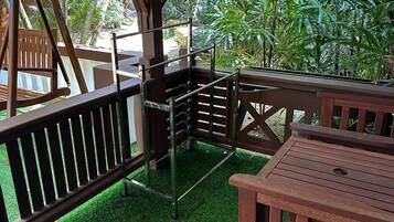 A covered outdoor seating area with wooden furniture and a view of lush greenery.