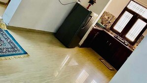 Una habitación amplia con piso de madera pulida, un mueble negro y una planta pequeña en la pared.