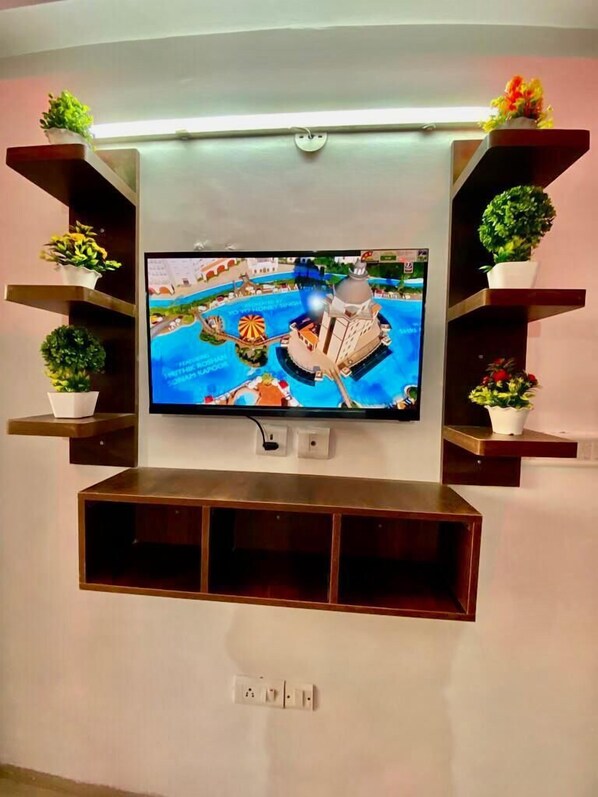 A flat-screen TV mounted on a wall with wooden shelves on either side, each holding a potted plant. - Hotel & BNB Solanki Residency Jaipur (Jaipur)