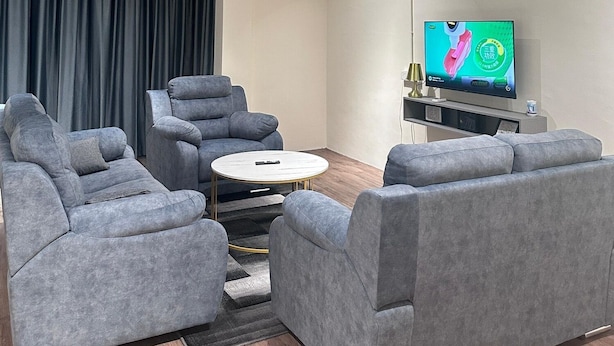 A modern living room with grey sofas, a round coffee table, and a flat-screen TV on a stand. - Leo66 Guesthouse  (Muar)