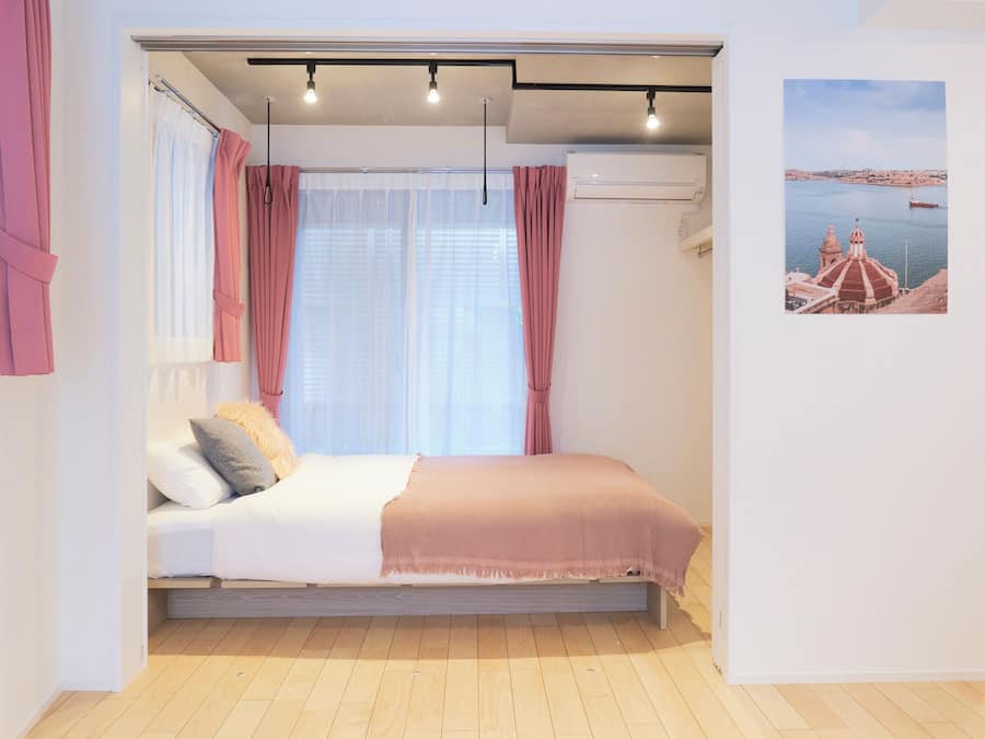 A bedroom with a bed, curtains, a window, and a wall-mounted air conditioner.