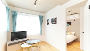 Una habitación moderna y bien iluminada con un televisor de pantalla plana, una mesa redonda con cubierta de mármol y una cama con colchón y almohadas blancos.