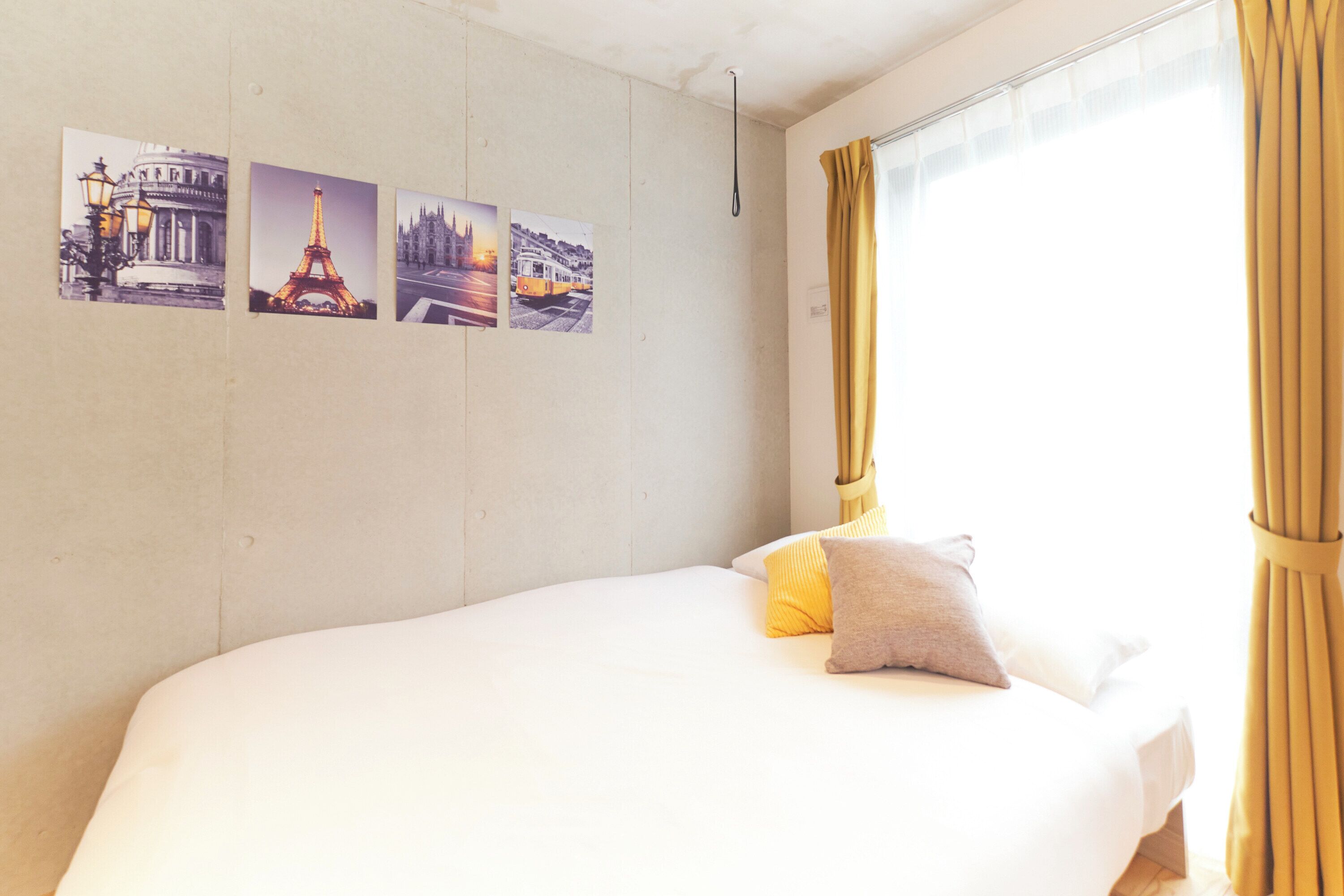 A bed with white bedding, a single pillow, and a window with yellow curtains.