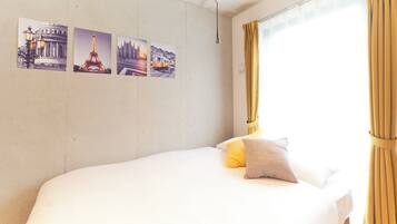 A bed with white bedding, a single pillow, and a window with yellow curtains.