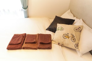 A bed with three folded towels, a pillow with a bicycle pattern, and a plain pillow.