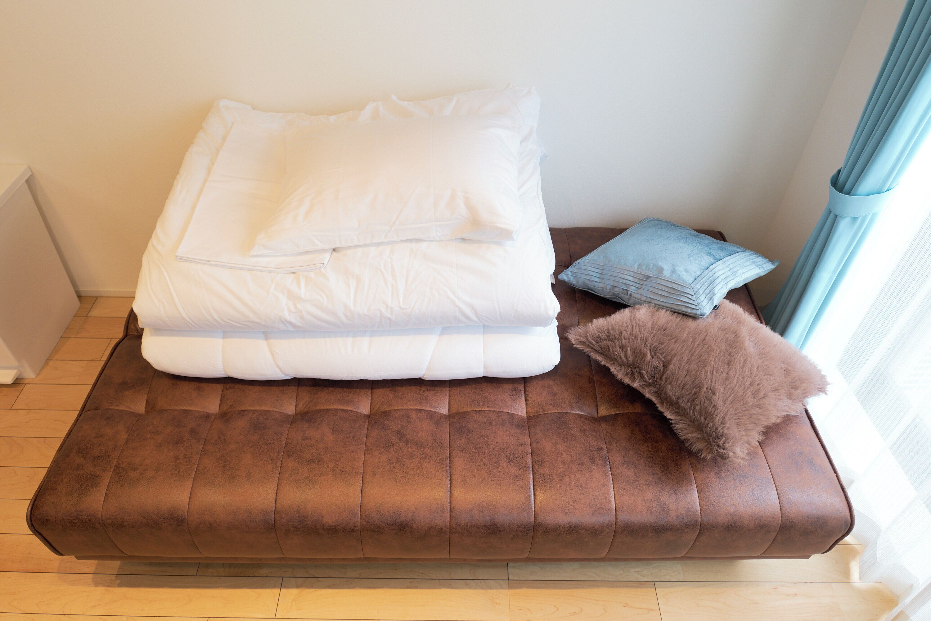 En brun soffa med en vit madrass och kuddar, en blå kudde och en brun fäll.
