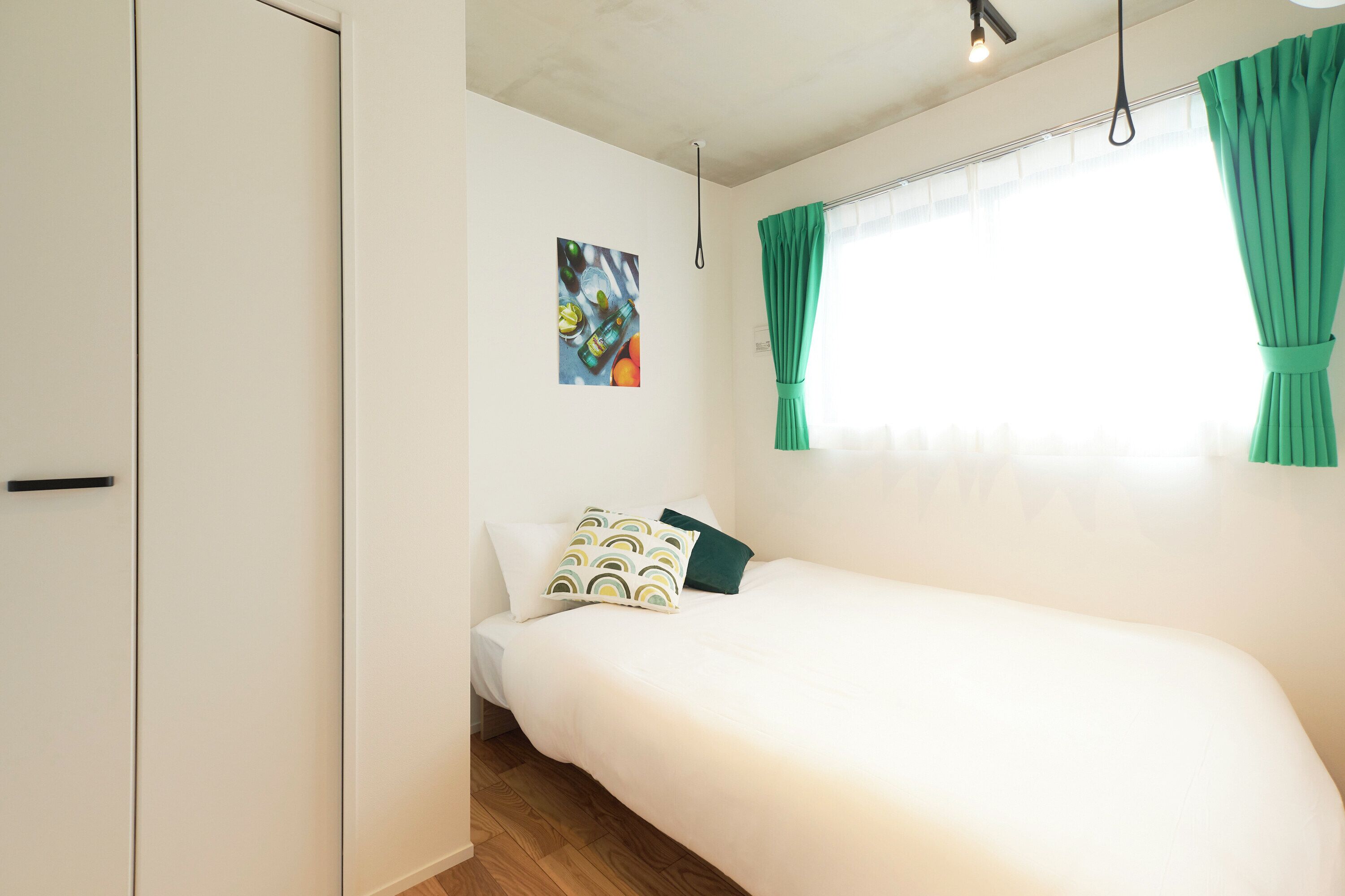 Un dormitorio con cama, una puerta, una ventana con cortinas e imagen colgada en la pared.