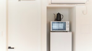 Una kitchenette compacta con microondas y cafetera sobre un refrigerador pequeño.