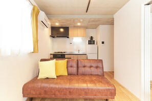 Um espaço compacto para viver, com sofá, cozinha e mesa de jantar.