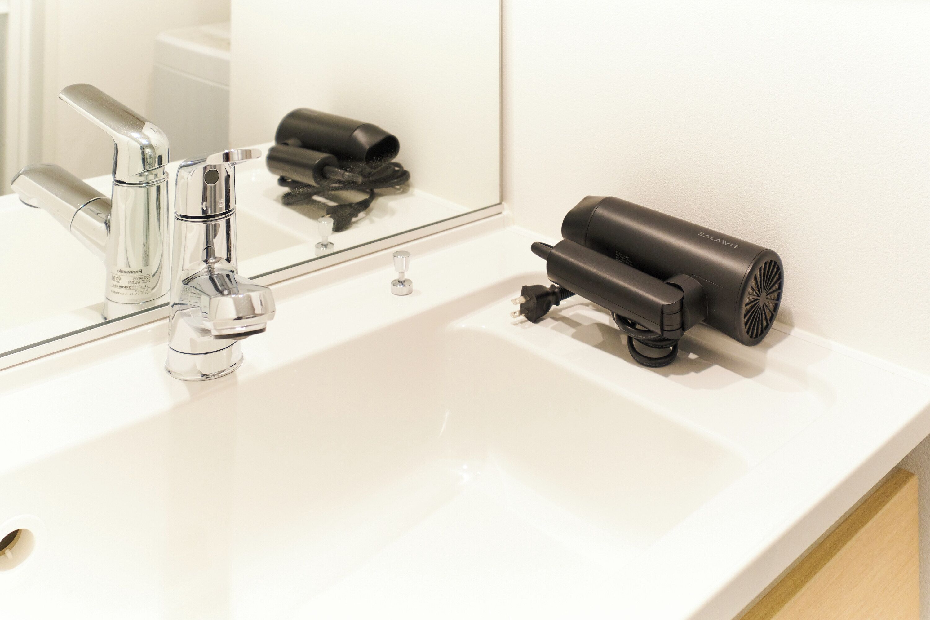 A bathroom with a white sink, a mirror, and a hairdryer.