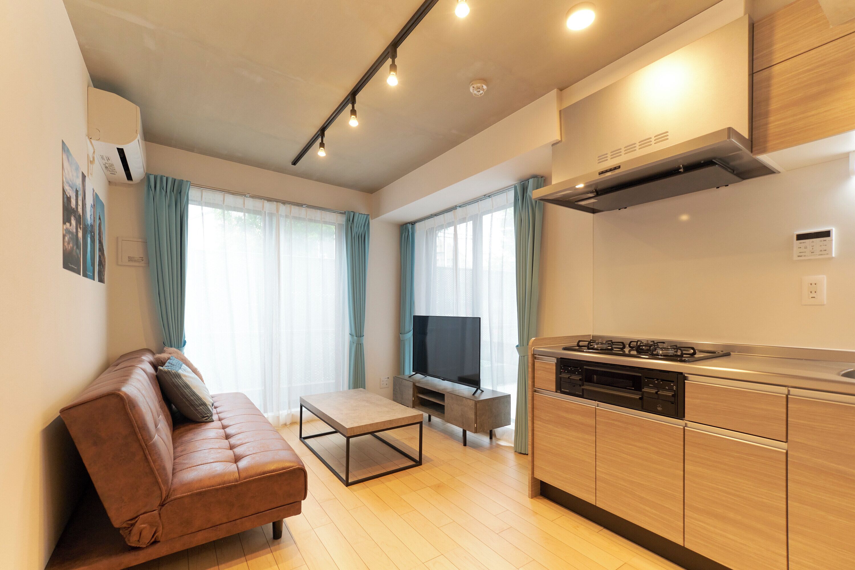 A modern living room with a sofa, coffee table, TV, and kitchen area with cabinets and a stove.