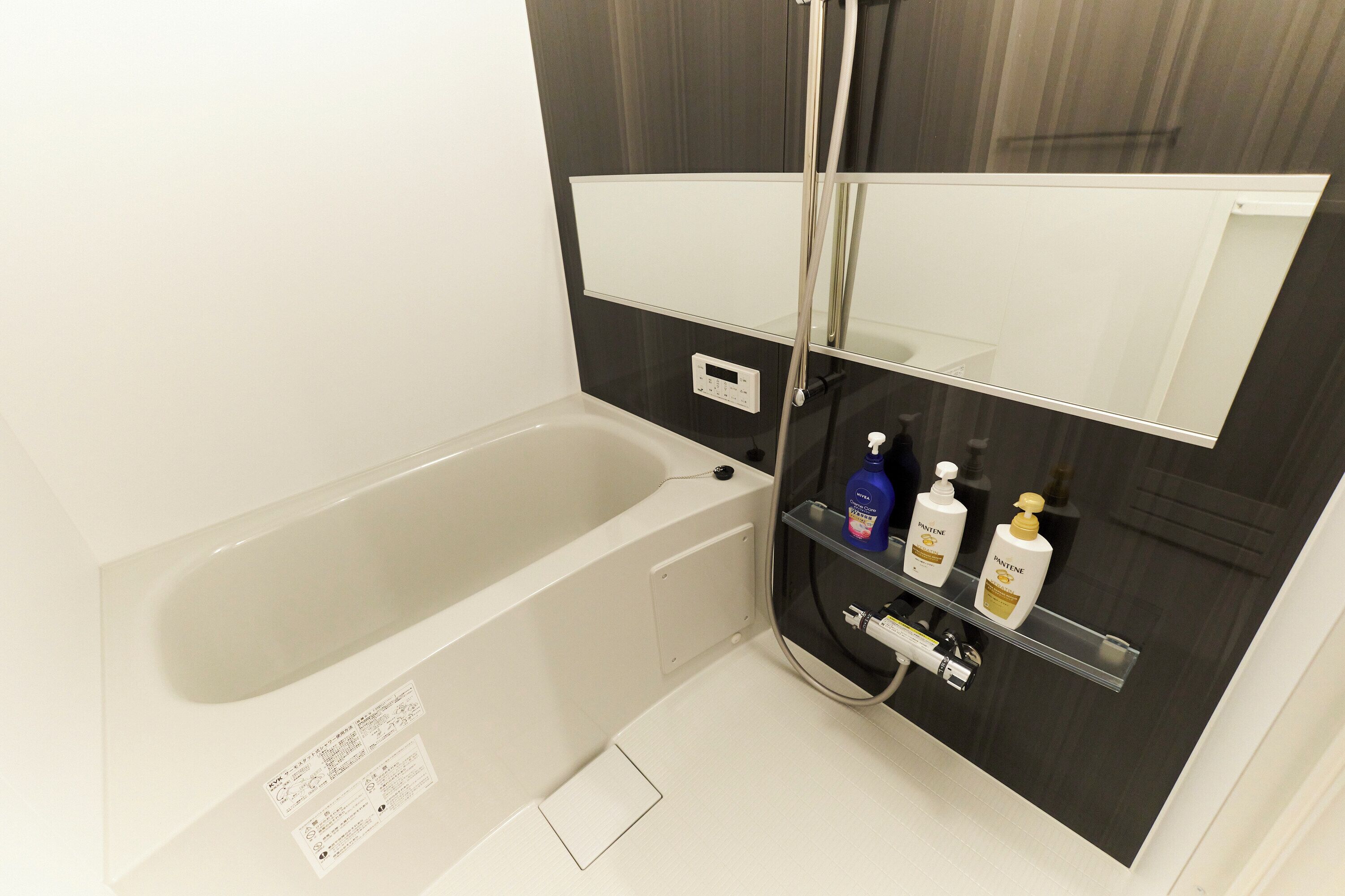 A bathroom with a bathtub, a mirror, and a shelf with toiletries.