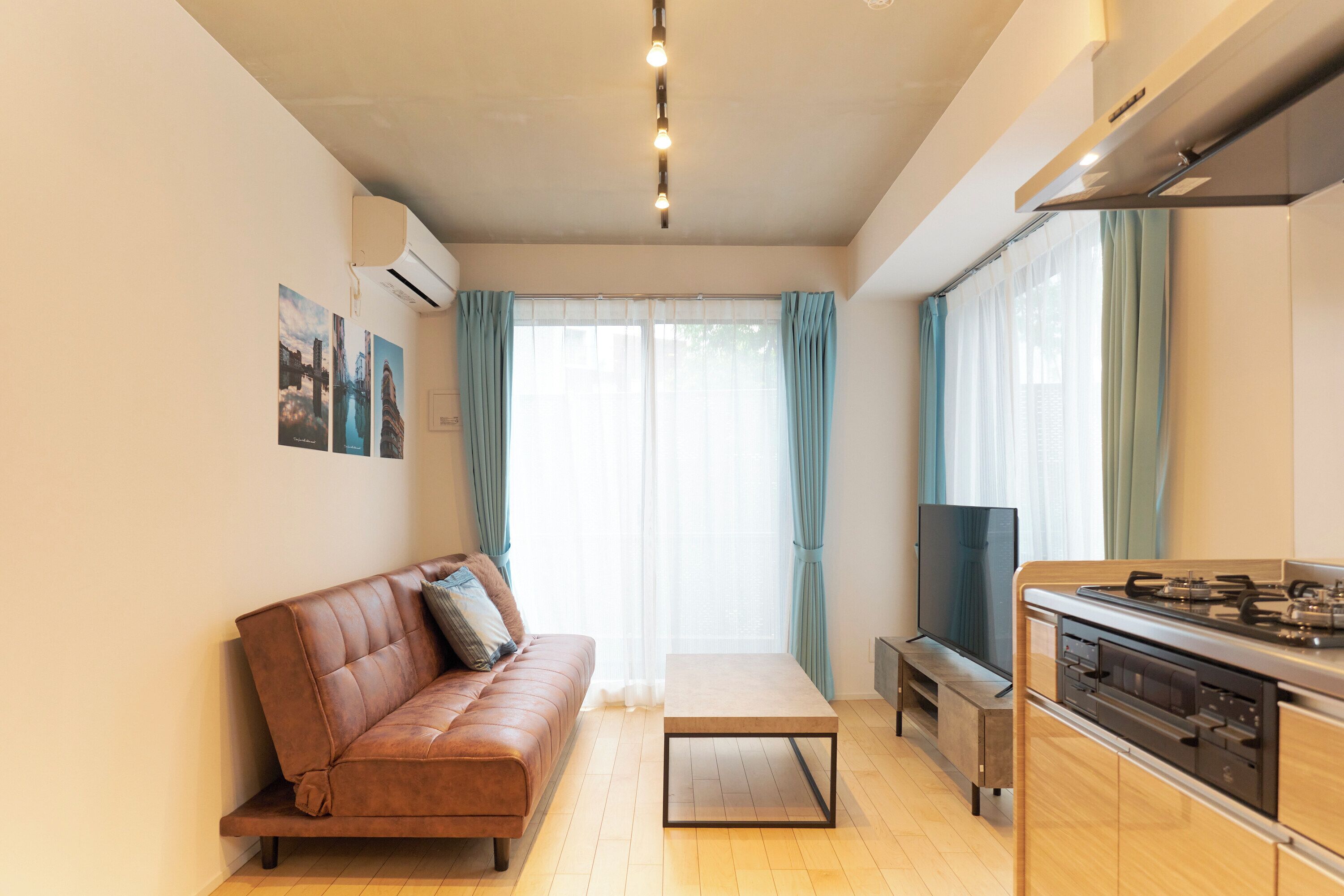 A modern living room with a sofa, a coffee table, a TV, and a kitchen area with a stove.