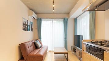 A modern living room with a sofa, a coffee table, a TV, and a kitchen area with a stove.