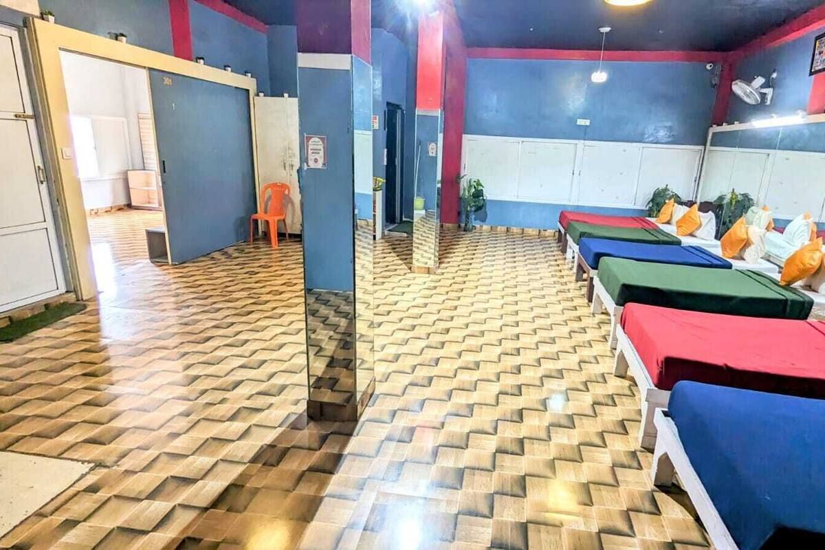 A room with a patterned floor, multiple beds with colorful bedding, and a mirror reflecting the room.