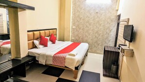 A hotel room with a bed, a TV, a desk, and a patterned wall. - Hotel Jee (Varanasi)