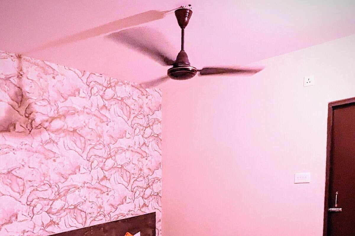 A neatly made bed with orange bedding, a ceiling fan, and a patterned wall.