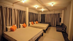 A hotel room with two beds, a sofa, and a patterned ottoman. - Hotel Jee (Varanasi)