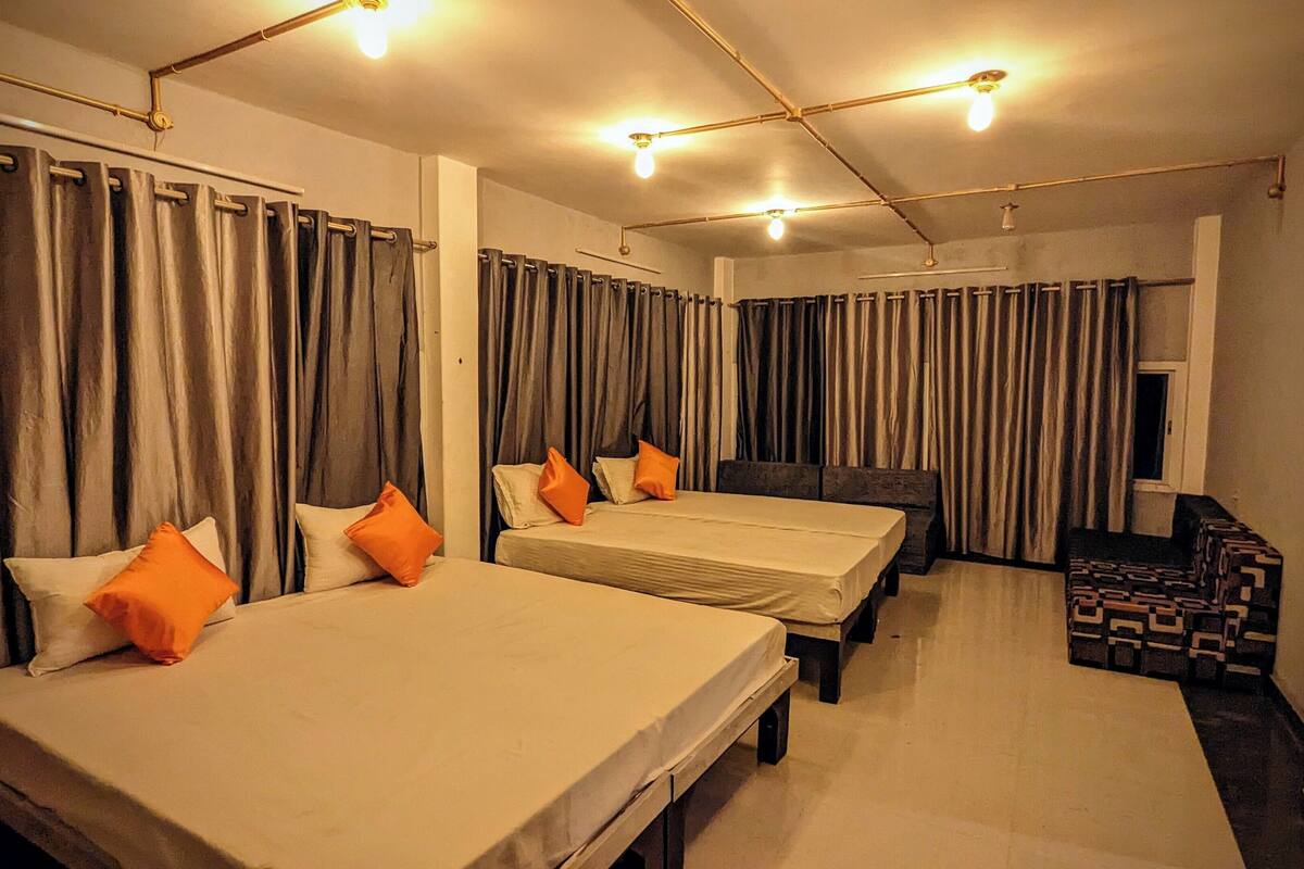 A hotel room with two beds, a sofa, and a patterned ottoman.