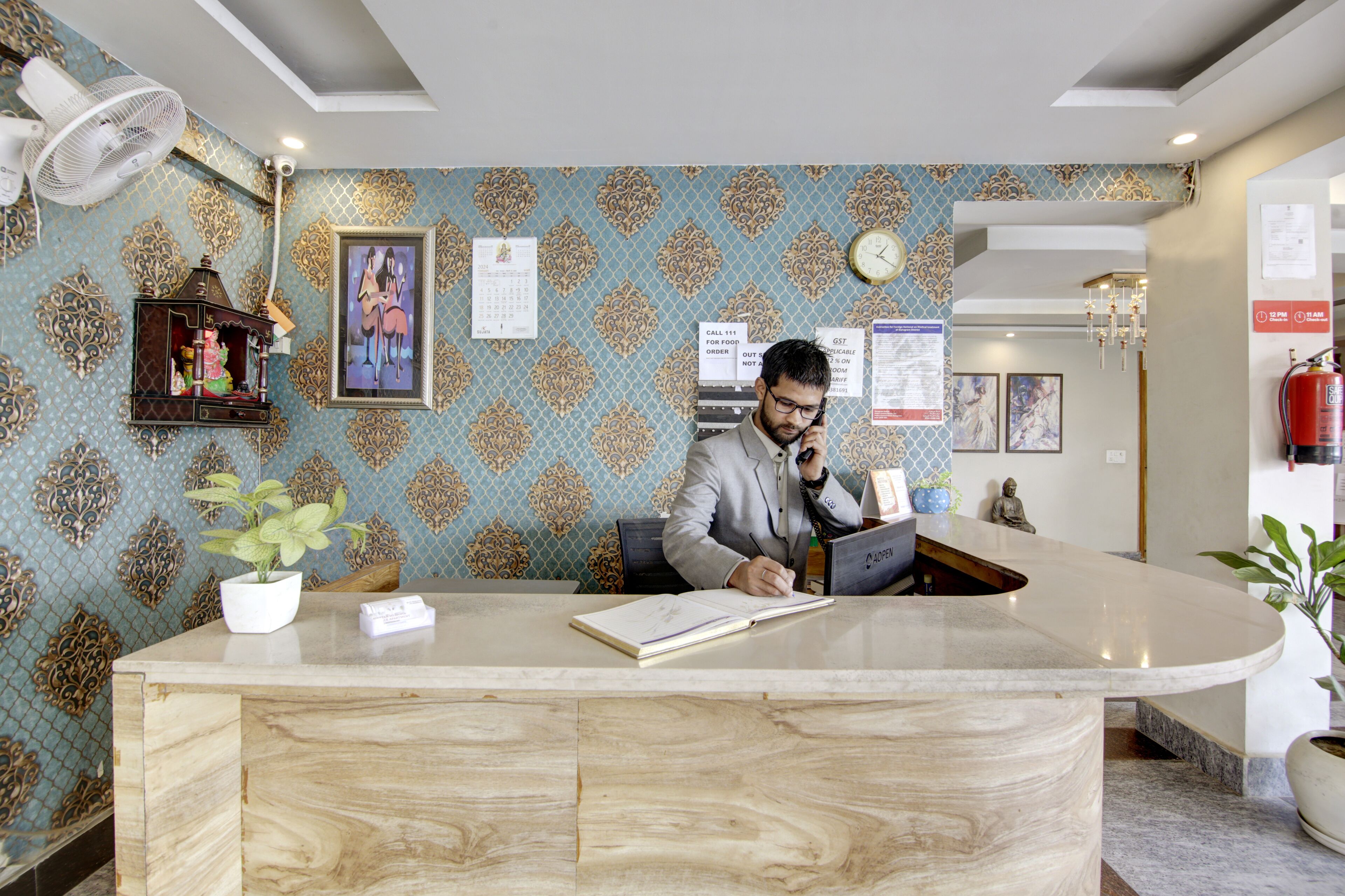 Un comptoir d’accueil avec un plateau en marbre, une plante en pot et un calendrier accroché au mur.