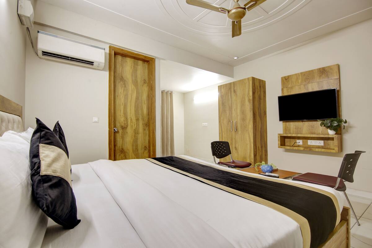 Una habitación de hotel con una cama, un escritorio, una silla, aire acondicionado, ventilador de techo y un televisor montado en la pared.