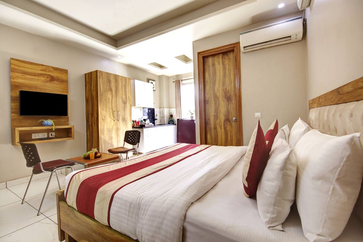 Un dormitorio con cama, televisión montada en la pared, escritorio con silla y armario.