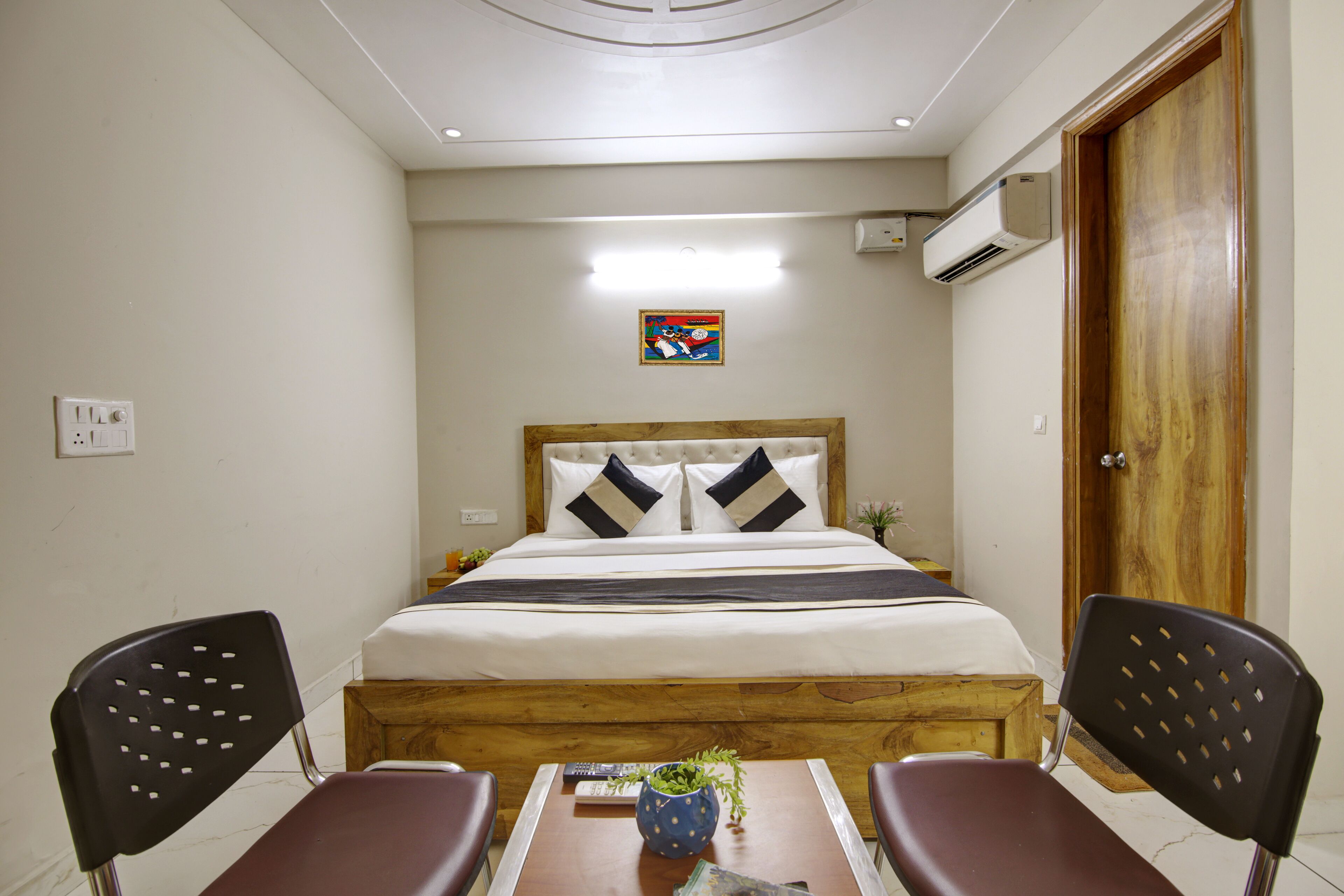 A hotel room with a bed, two chairs, a table, and a wall-mounted air conditioner.