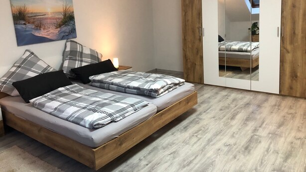 A bedroom with a bed, bedside tables, a nightstand, a mirror, and a wardrobe.